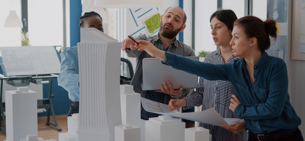 Group of colleagues meeting to analyze building model and maquette to plan blueprints