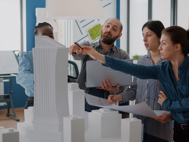 Group of colleagues meeting to analyze building model and maquette to plan blueprints