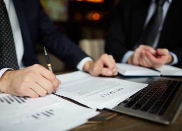 Closeup portrait of unrecognizable successful businessman wearing black formal suit reviewing documents and signing contract during meeting